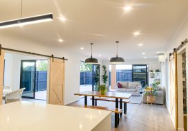 Bright modern living room with neutral decor, indoor plants, and sliding glass doors overlooking the backyard.