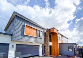 Contemporary modern house with grey siding, wood accents, and stone feature wall in Auckland, New Zealand.