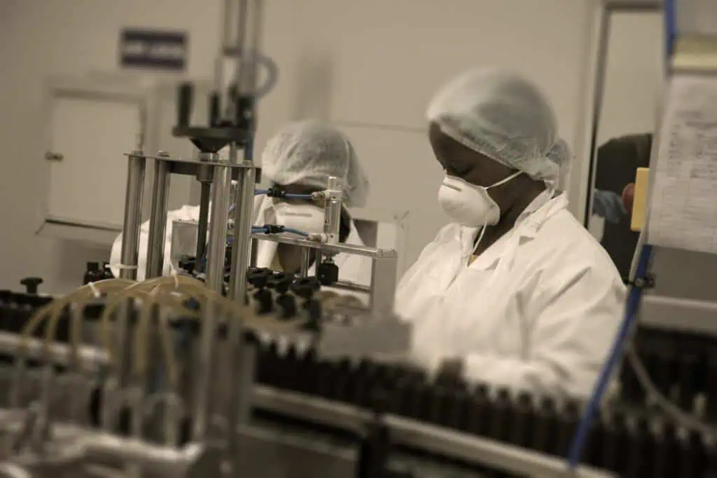 Workers in protective gear inspecting pharmaceutical production line.