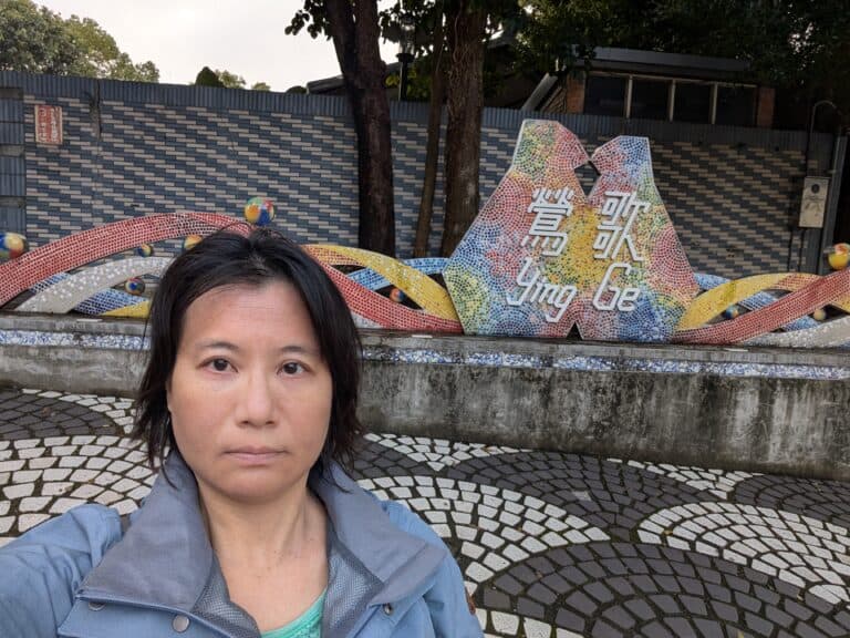 ALT：一位女性在大漢溪左岸自行車道附近的彩色藝術裝置前拍照，背景是樹林水源街口和鶯歌陶博館，展現自然與文化融合的景觀。.