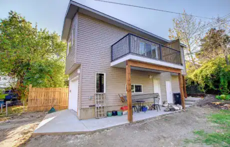 Two-storey house featuring a small balcony, beige siding, and outdoor patio with seating.