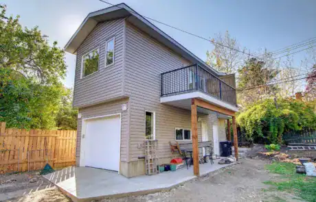 Bright, new siding house with balcony, outdoor seating, and lush garden surroundings.