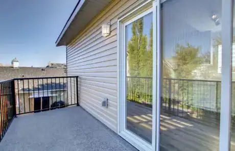 Balcony outdoor space with sliding glass door, view of neighborhood, safety railing, exterior lighting.
