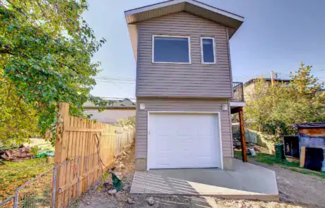 Bright, new house with a garage, second story, and outdoor balcony, surrounded by trees.