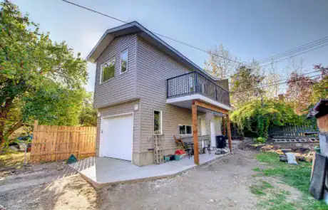 Bright, inviting house with siding, balcony, and outdoor seating area, surrounded by trees.