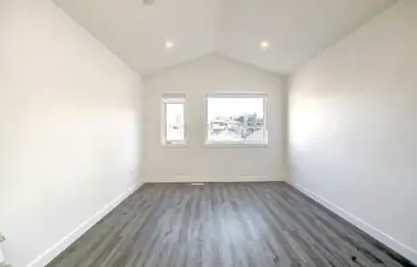 Bright, spacious bedroom with natural light, white walls, and sleek wood floors in a contemporary home.