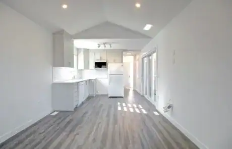 Bright minimalist kitchen with white cabinets and wood flooring in open-plan home.