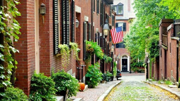 Historic cobblestone Beacon Hill street in Boston with brick rowhouses and U.S. flag — contact Gavagan Law, Boston personal injury attorney