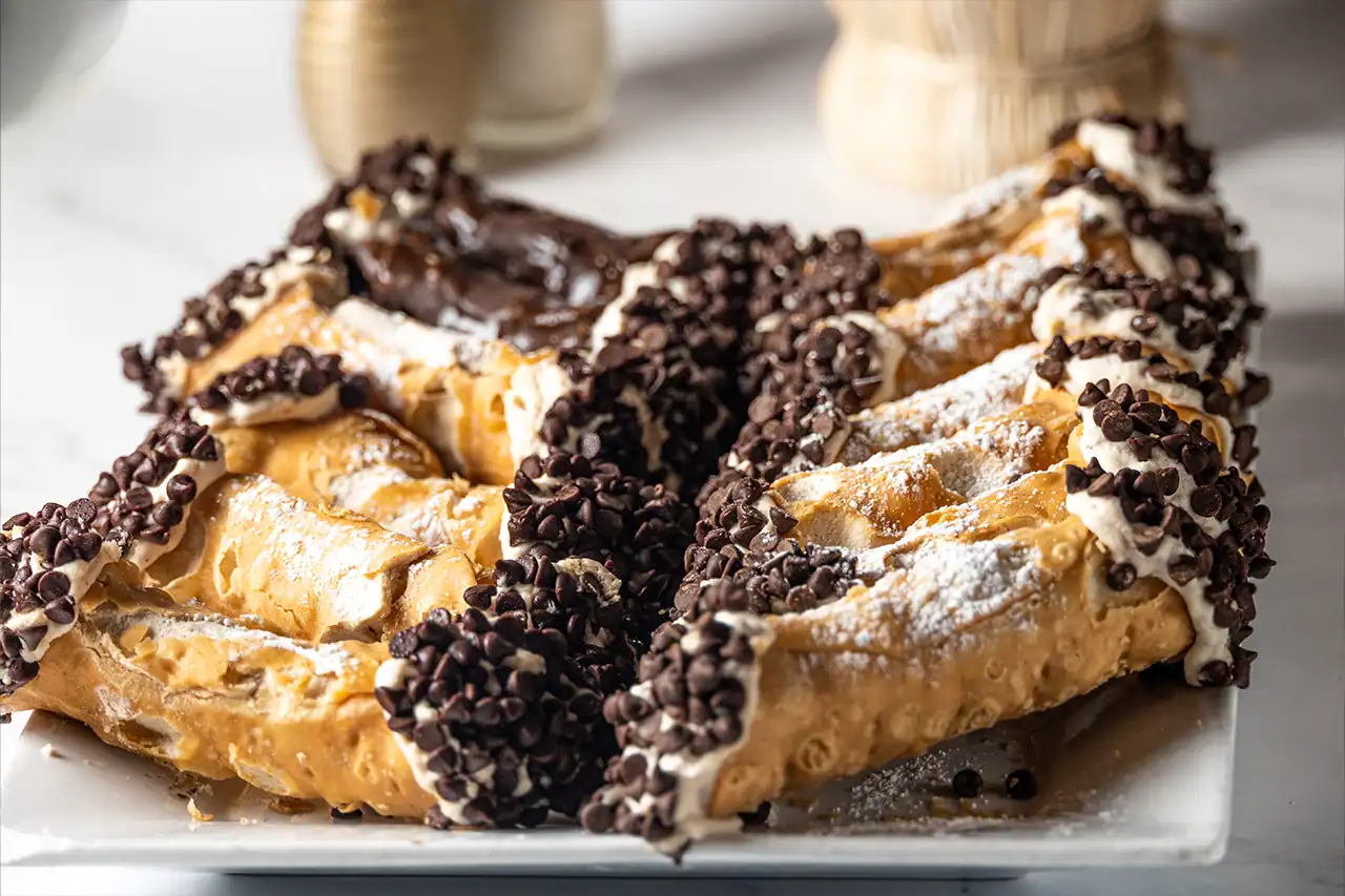 Chocolate chip cannoli dusted with powdered sugar on a serving plate