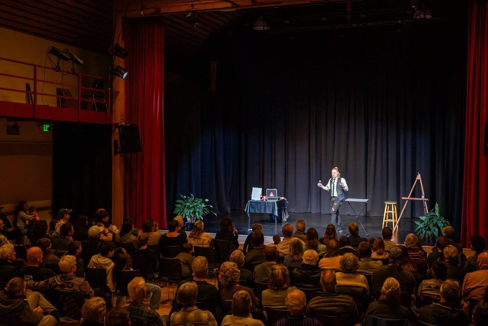 Side view of magician Henry Oz performing for a packed audience during a theater show on Lopez Island