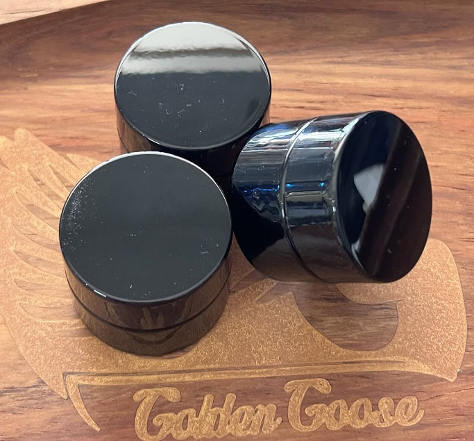 Black skincare jars on wooden surface, luxury beauty product display.