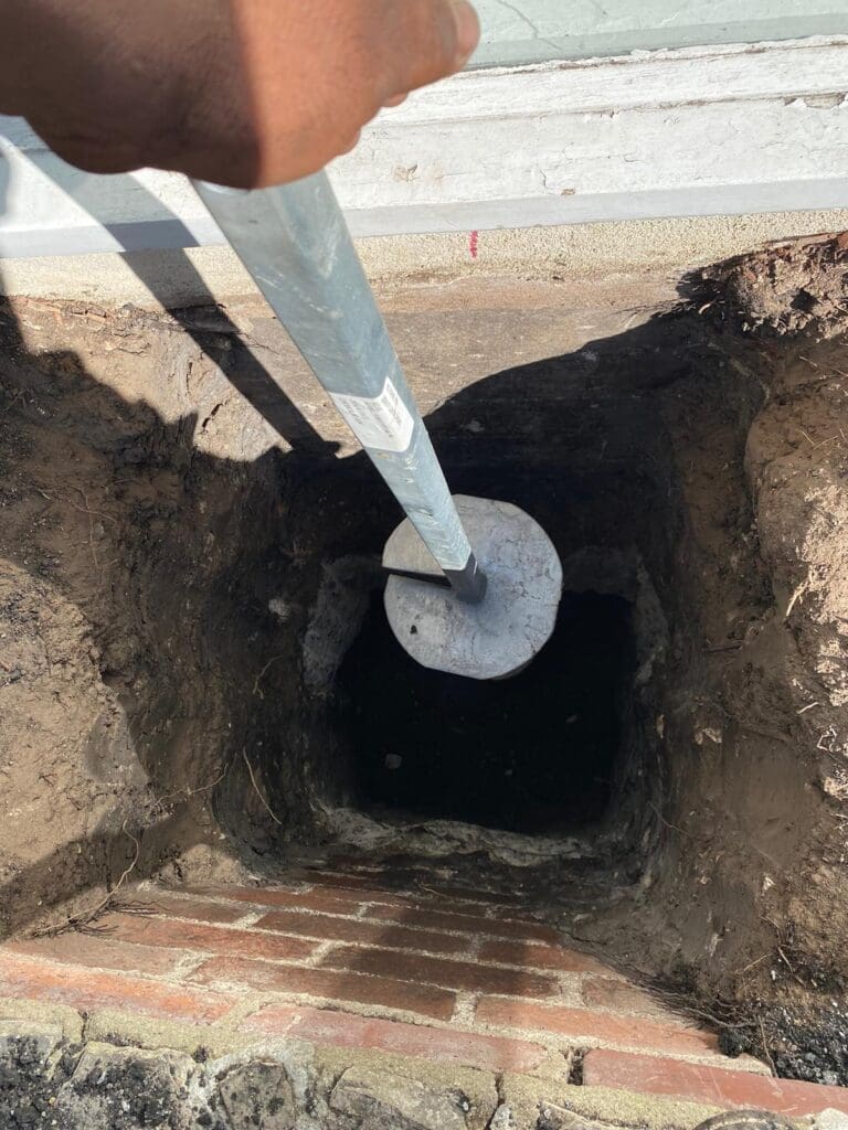 Person installing a helical pier into a deep hole next to a brick wall.