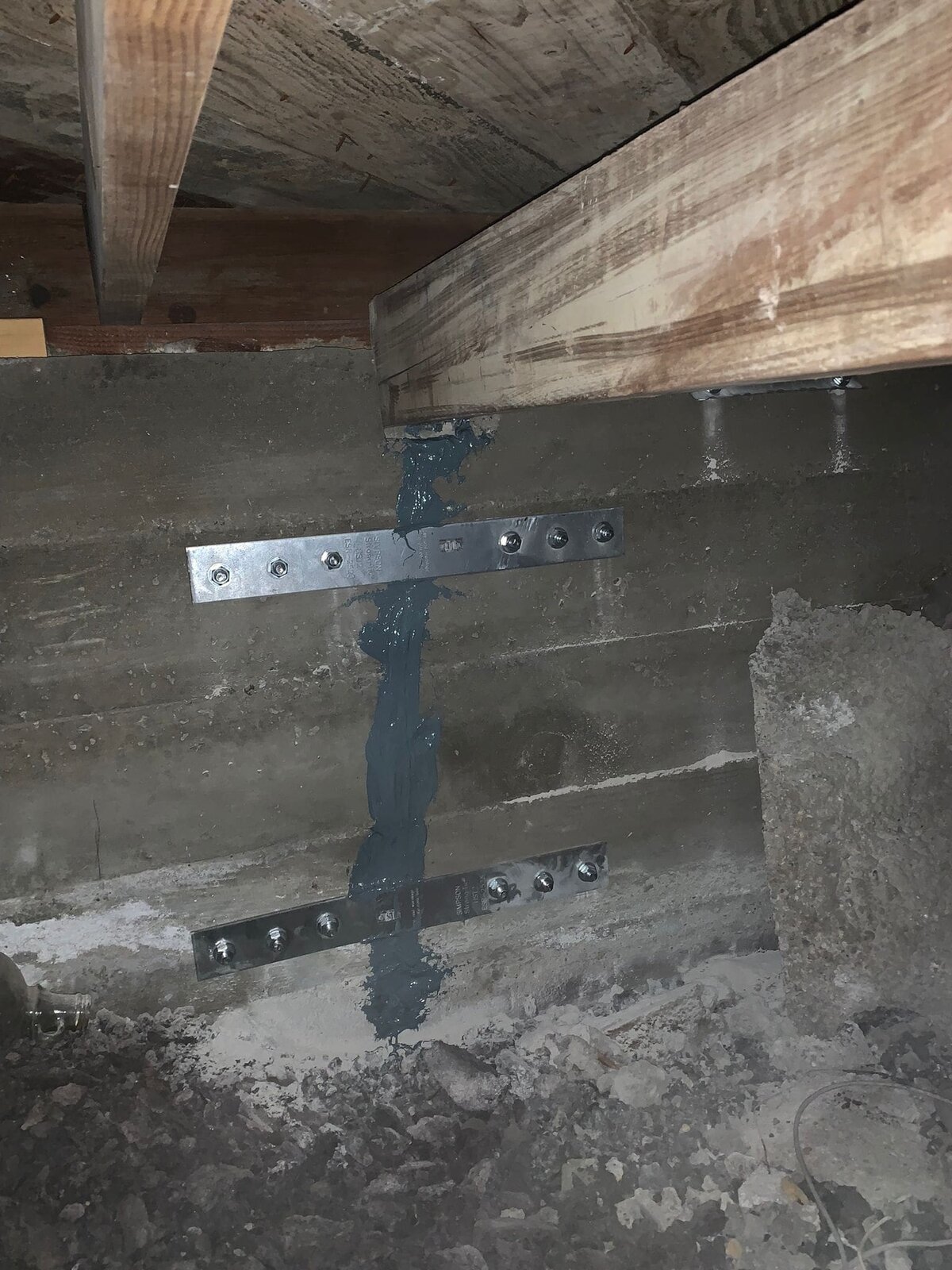 Foundation repair with metal plates, bolts, and sealant on a concrete wall.