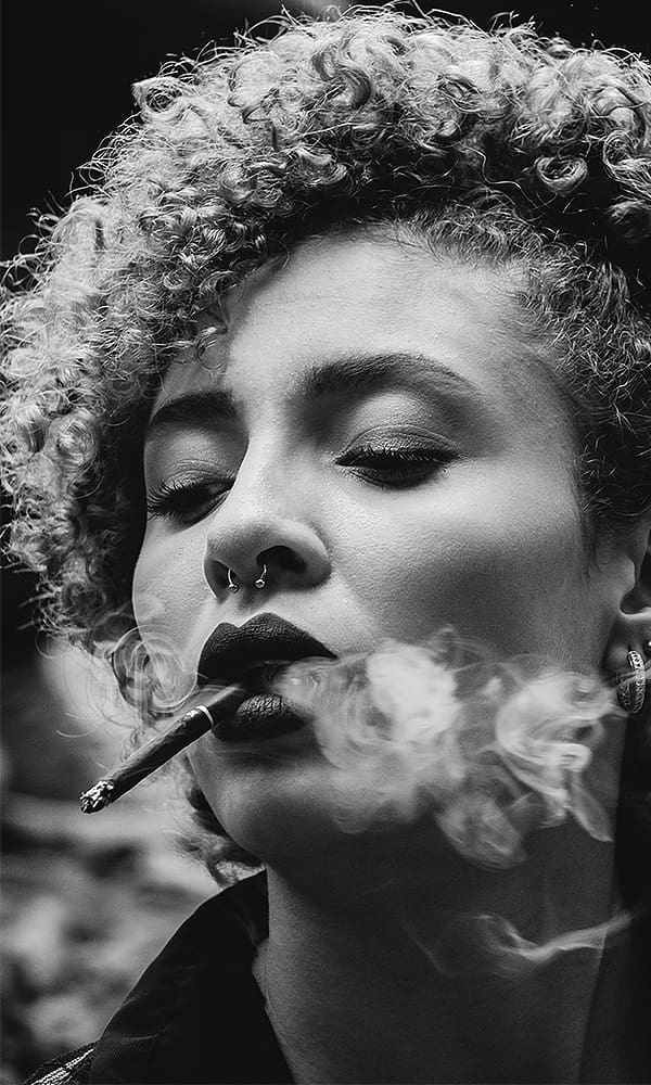 Black and white close-up of a woman with curly hair smoking a cigar