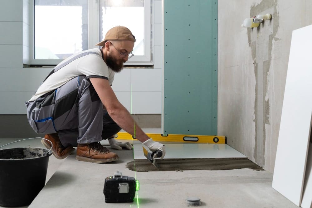 Man installing tiles on a floor with a laser level and tools