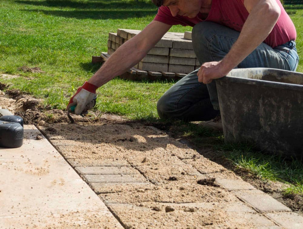 Man installing paving stones in a garden path on a sunny day