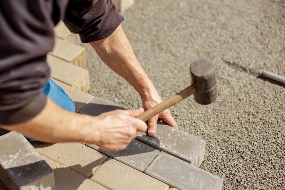 Person using a rubber mallet to lay paving stones on a gravel base.