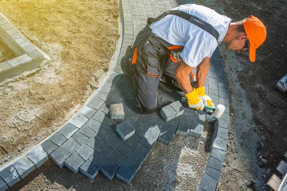 Man installing gray pavers for a garden path on a sunny day