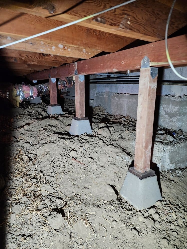 Crawl space with wooden support beams, concrete piers, and exposed dirt.
