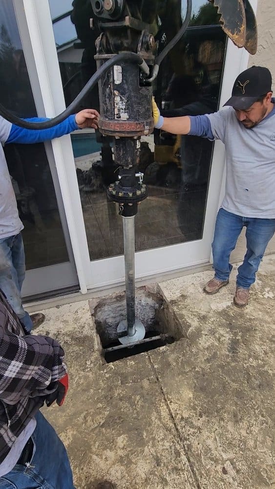 Two men operating a drilling machine to install a metal pole into the ground.