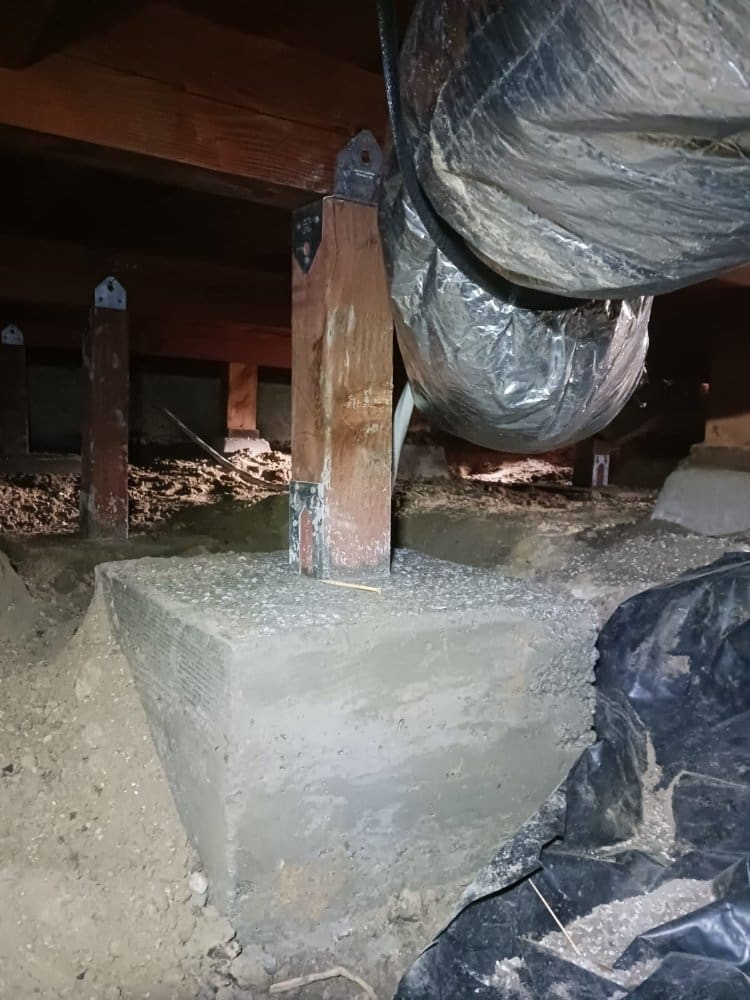 Wooden support beam on a concrete footing in a crawl space.
