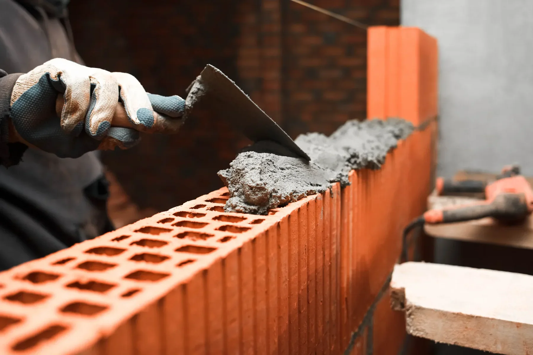 Close-up of a person's gloved hand applying mortar to a brick wall.
