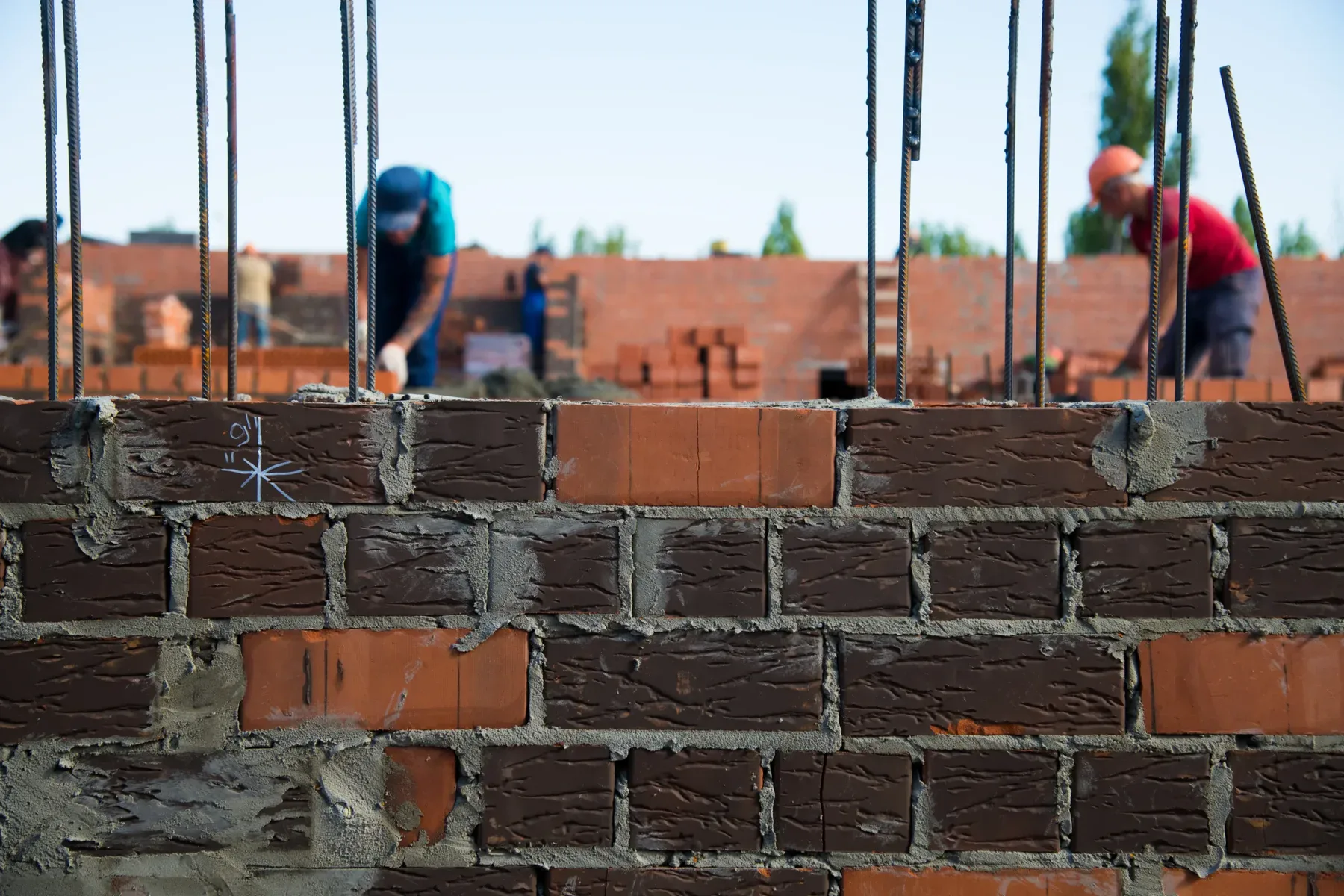 Close-up of a brick wall under construction with blurred workers in the background.