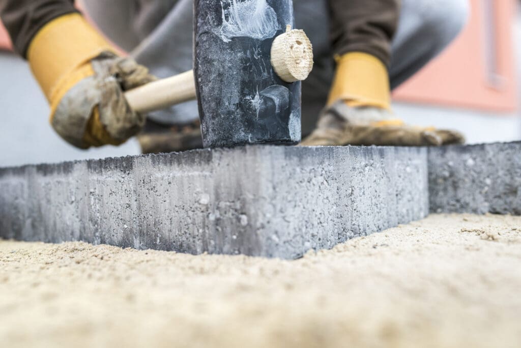 Person in work gloves using a mallet to tap a concrete paver into place.