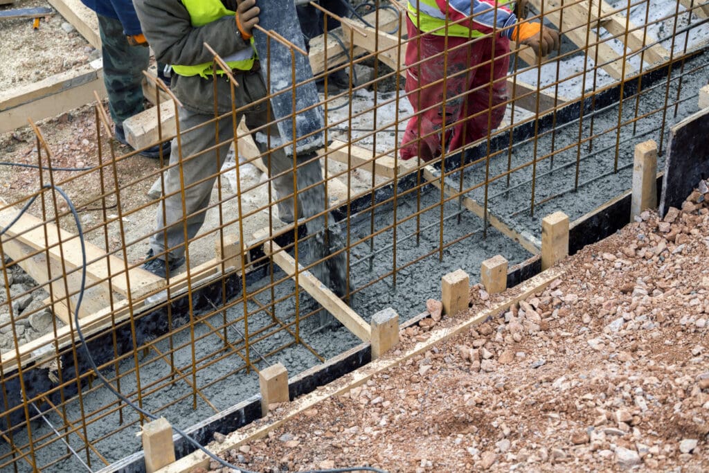 Workers pouring concrete into a foundation with rebar and wooden forms.