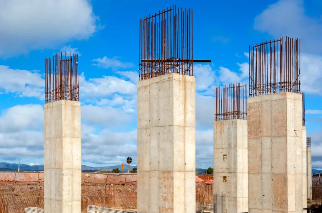 Four concrete pillars with rebar against a blue sky with clouds.