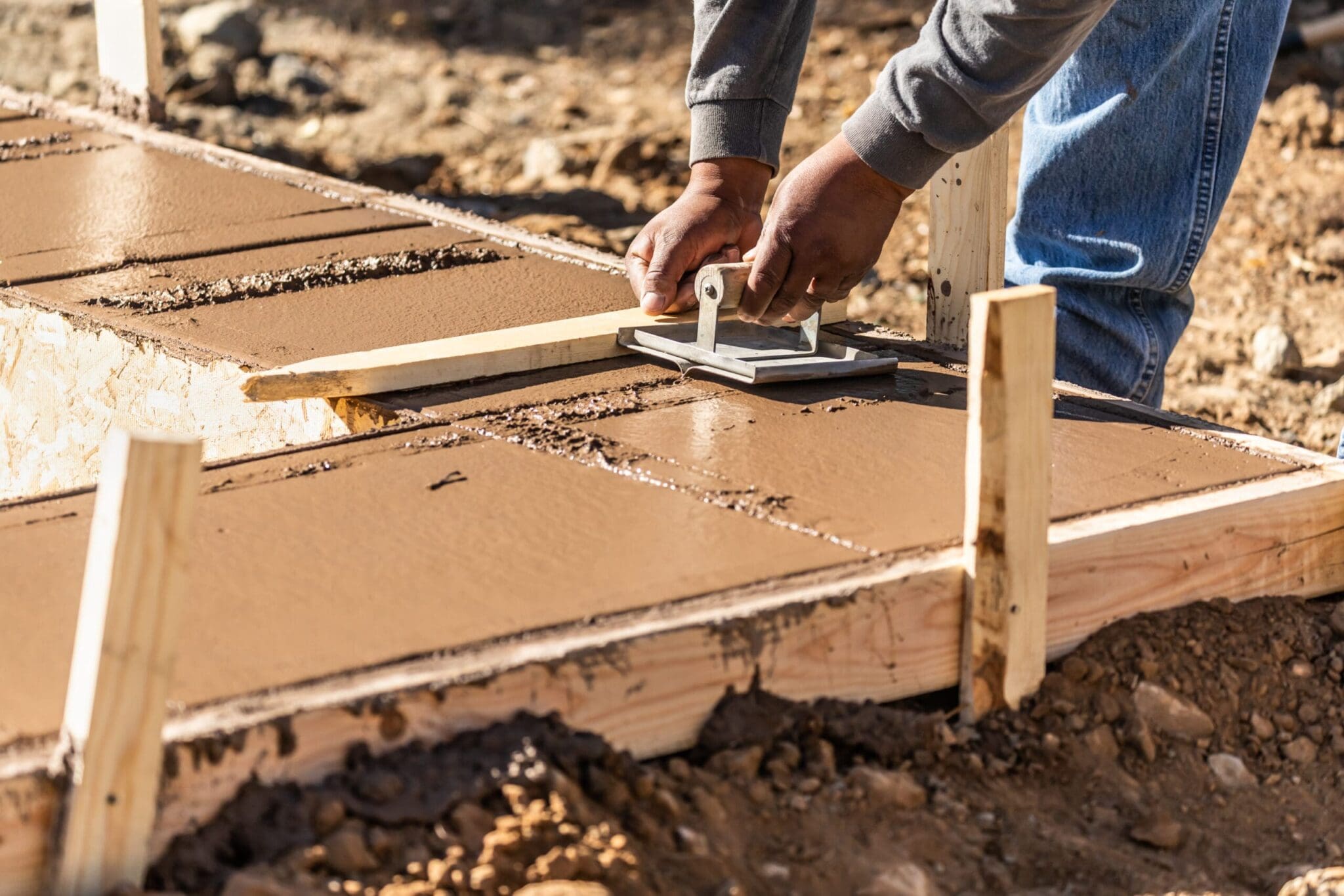 Person smoothing wet concrete with a hand float on a sunny day.