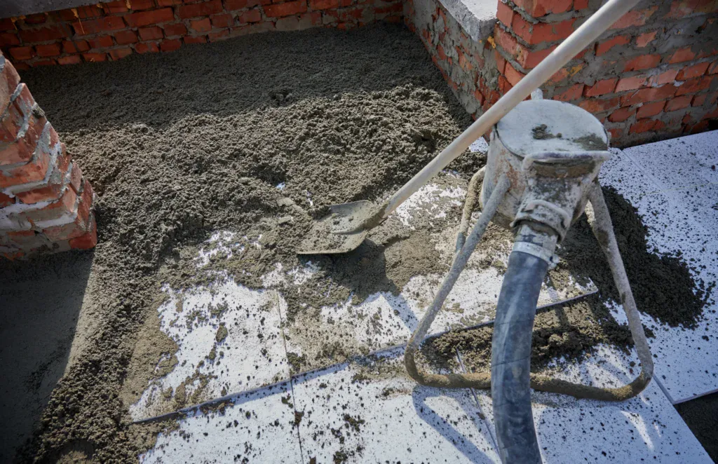Construction worker using a shovel to spread fresh concrete on a floor.