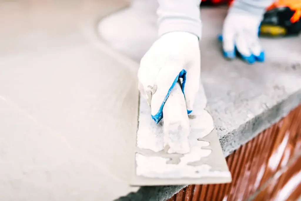 Close-up of a person's gloved hands applying mortar with a trowel.