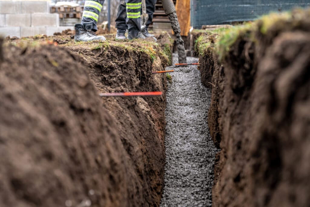 Workers pouring concrete into a narrow trench for a foundation.