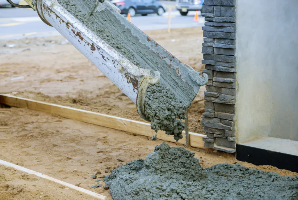Concrete being poured from a chute onto a dirt ground