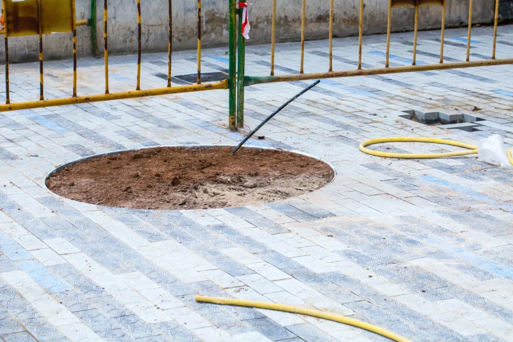 Round hole in paved ground with dirt, surrounded by construction barriers.