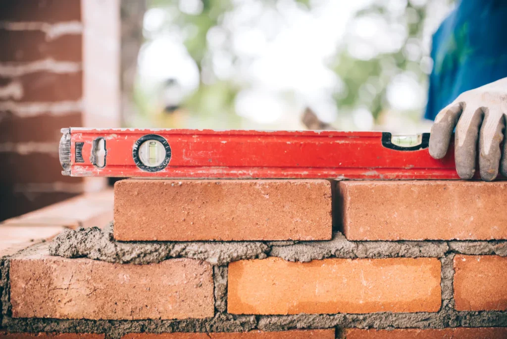 A person's gloved hand holding a red spirit level on a brick wall.