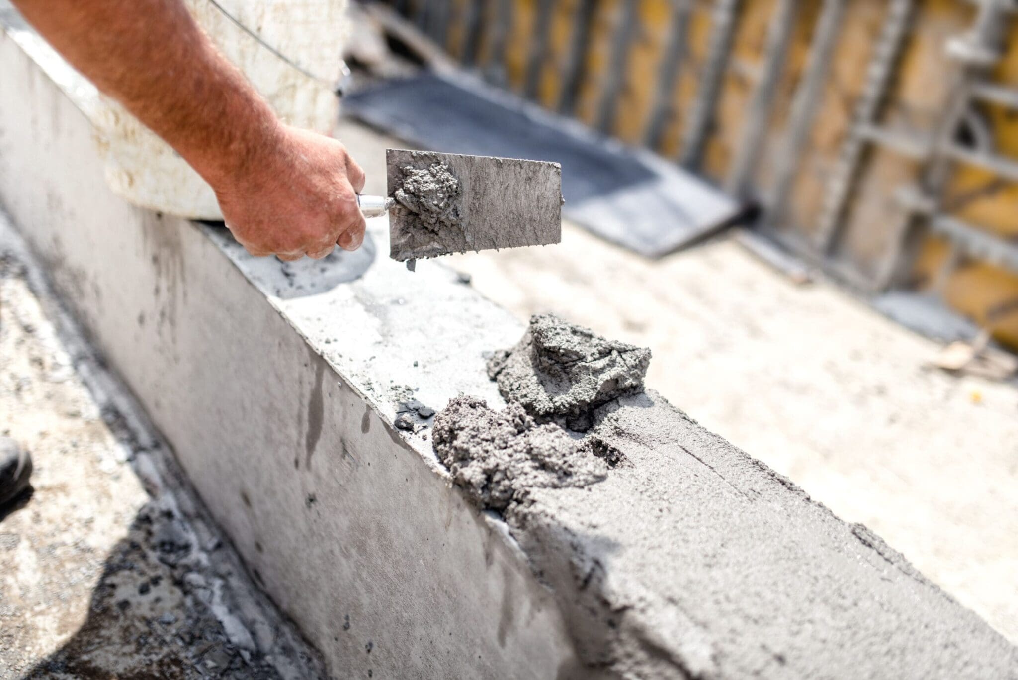 Close-up of a person's hand applying cement with a trowel.