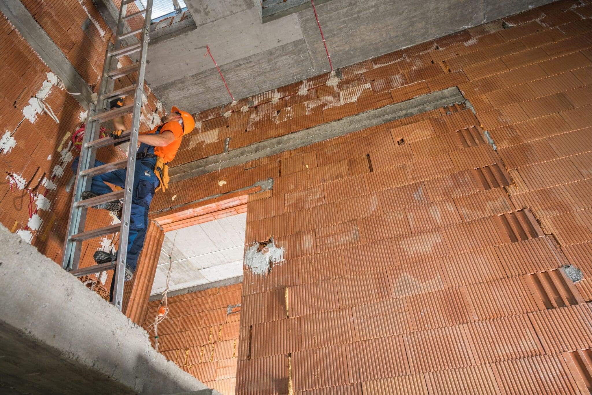 Construction worker on a ladder installing something on a brick wall