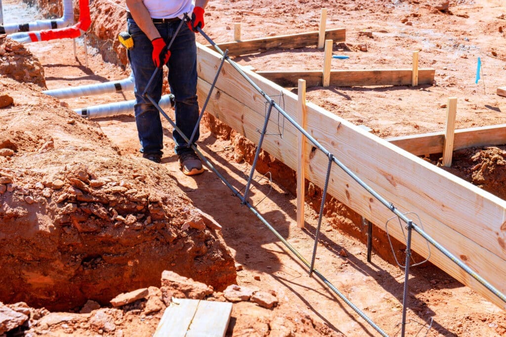 Construction worker in jeans and gloves standing on a dirt construction site.