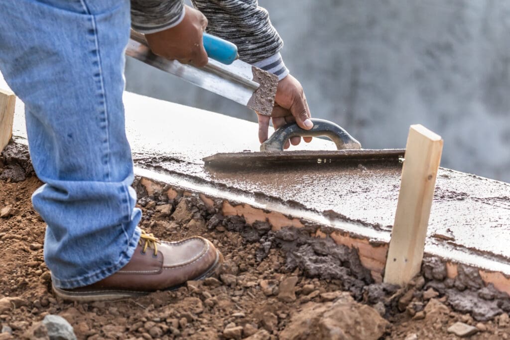 Person in jeans and work boots smoothing wet concrete with a trowel.