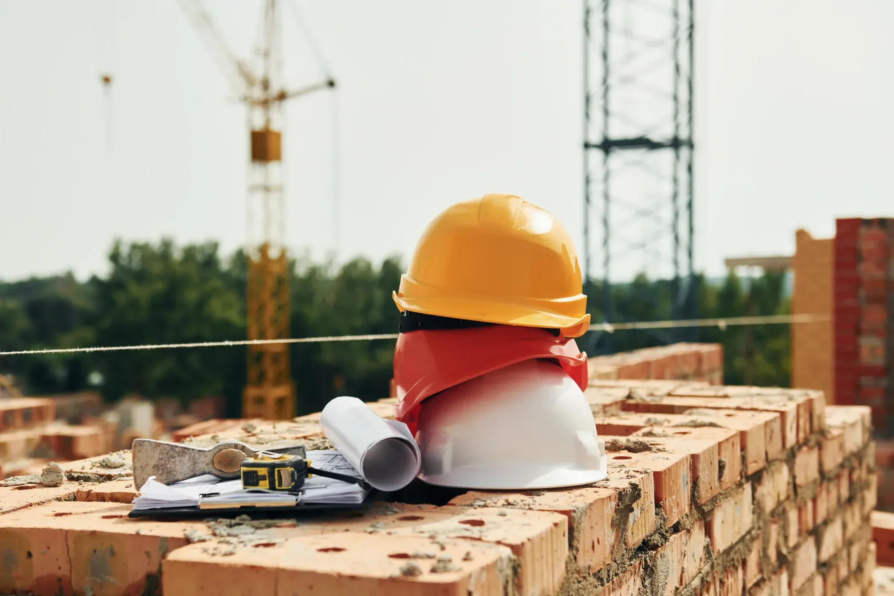 Stack of hard hats, clipboard, and axe on bricks at construction site.