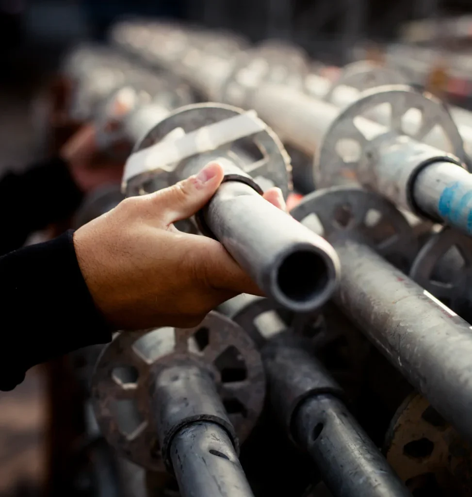 Close-up of a hand holding a metal scaffolding pole amidst a stack.