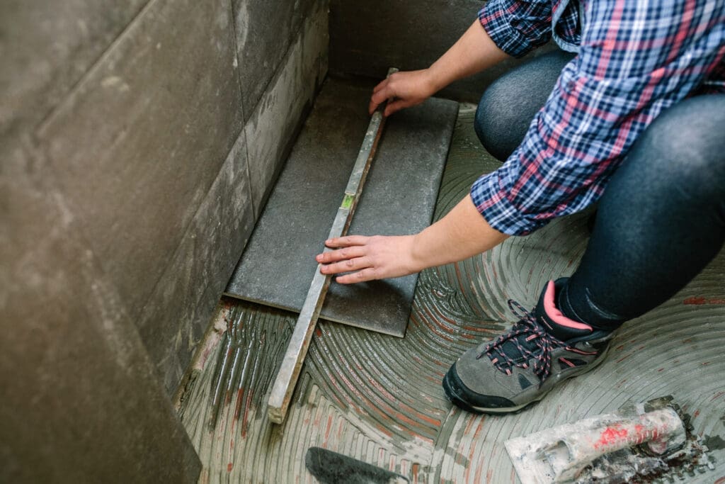 Person installing dark gray floor tiles with adhesive in a room.