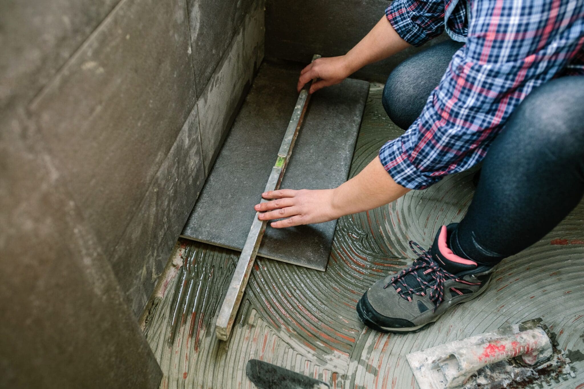 Person installing dark gray floor tiles with adhesive in a room.