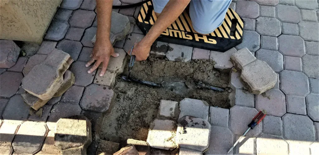 Person repairing a broken pipe under patio pavers.