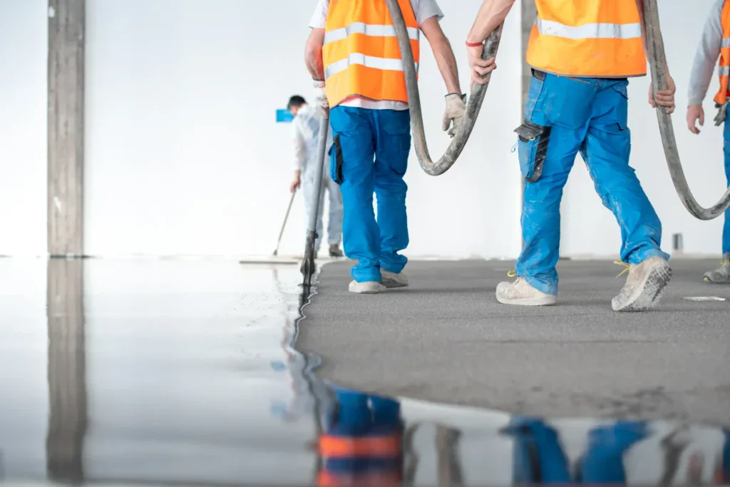 Workers in orange vests and blue pants applying floor screed