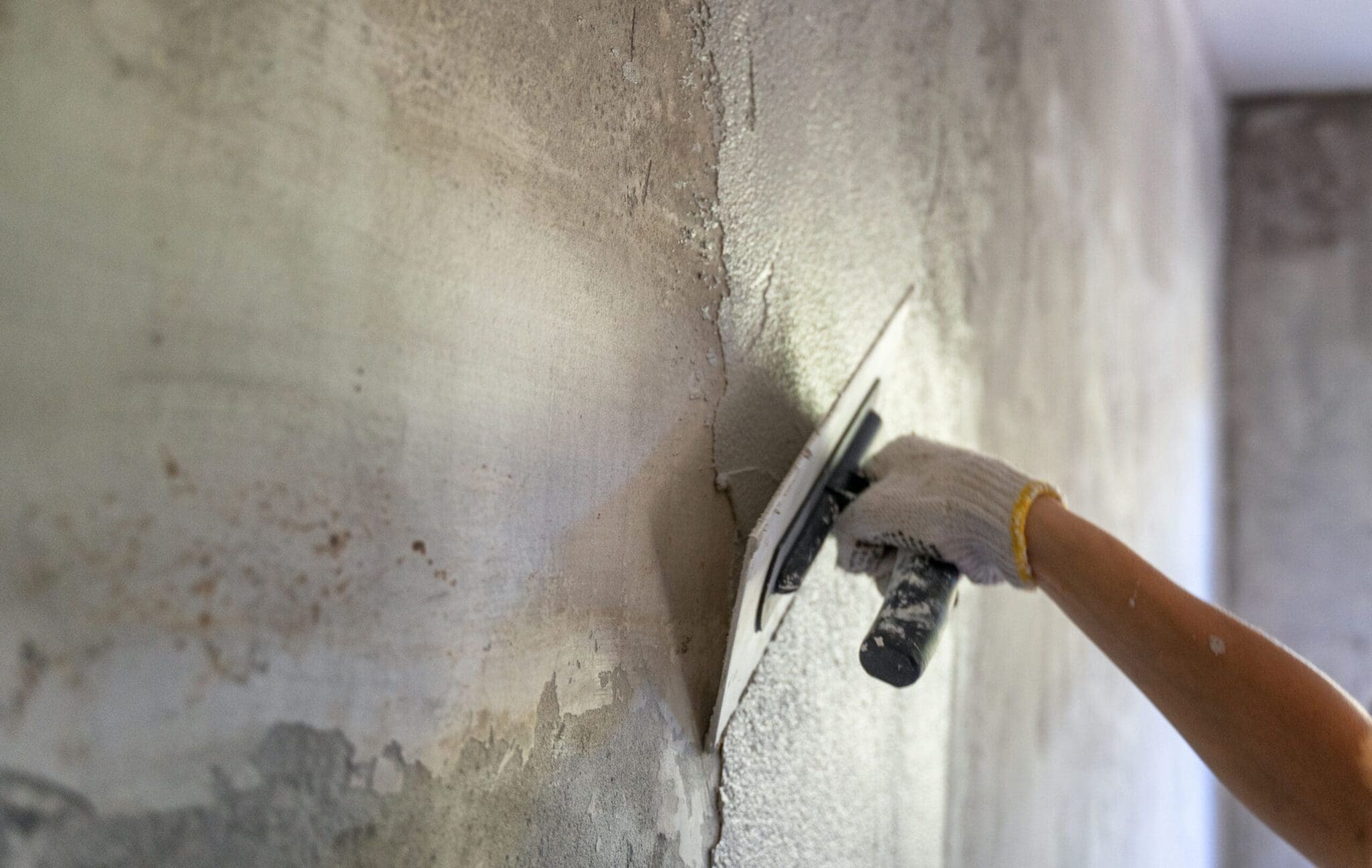 Hand in glove applying plaster to a wall corner with a trowel.