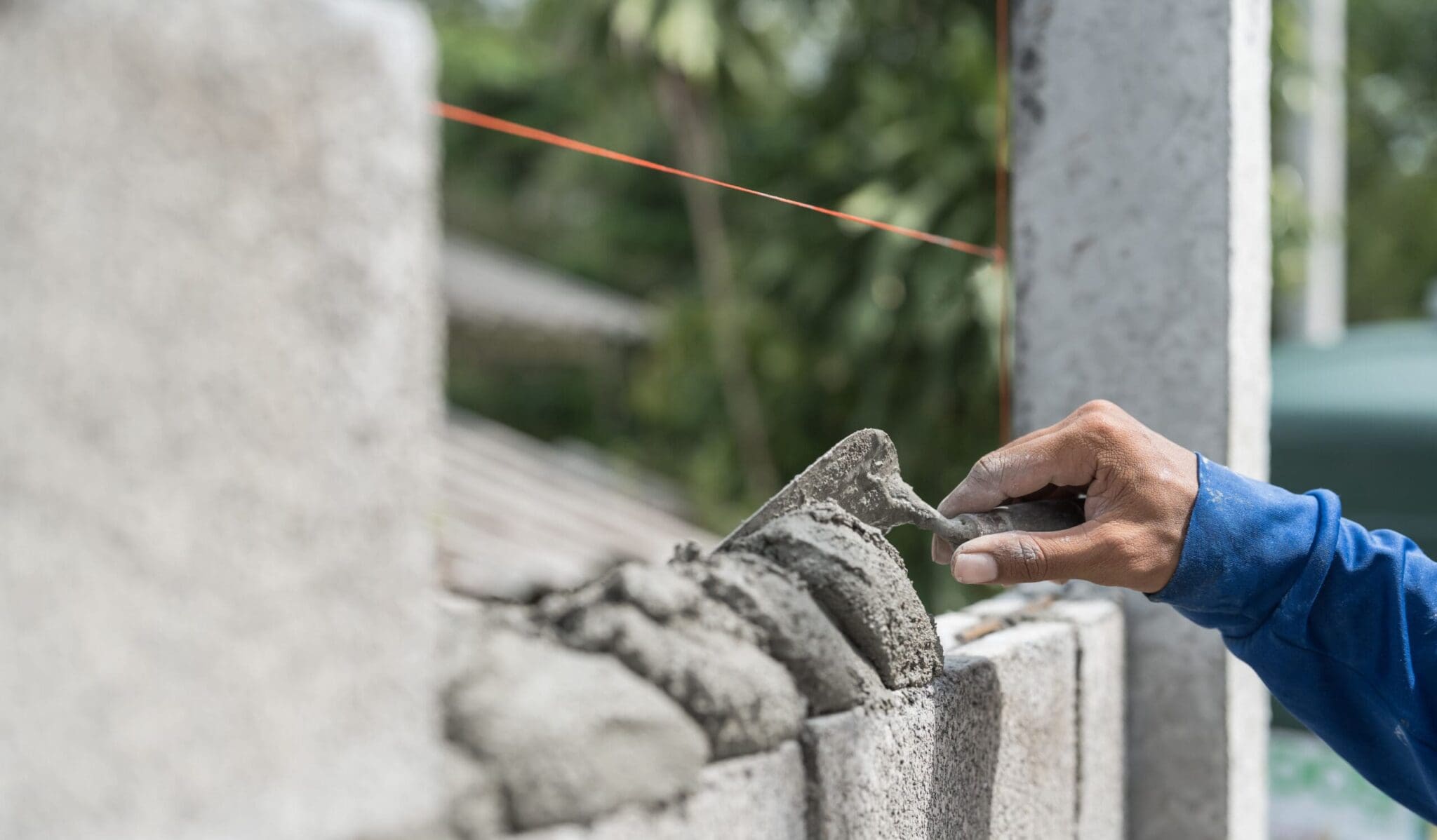 Close-up of a hand using a trowel to apply cement to concrete blocks.