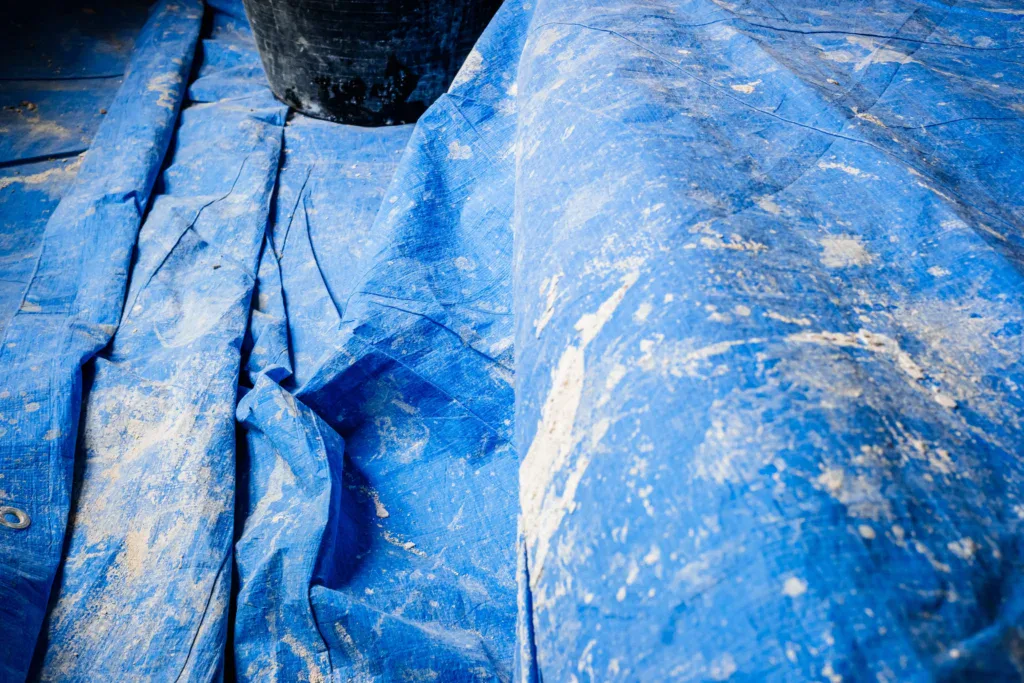 Close-up of a dirty blue tarp with white specks and a black bucket.